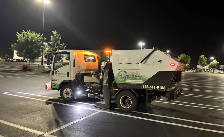 Green and Clean parking lot sweeper truck cleaning a retail center lot at night in Greensboro NC